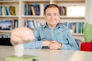 Professor Onur Güntürkün, a middle-aged white man with short hair, is sitting at a desk with his back to bookshelves. © RUB/Marquard