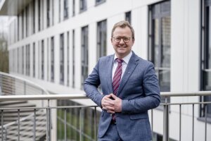 Ein Mann in Anzug und Krawatte (Niklas Thon) steht selbstbewusst vor einem modernen Gebäude. © RUB/Marquard