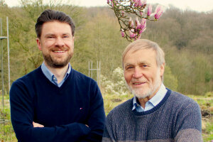 Two men standing in front of a tree with flowers in bloom. © Susanne Stachowitz