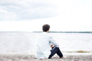 Ein Mann sitzt einsam am Strand und schaut aufs Wasser. © Pexels über Pixabay